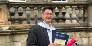 Alumnus Ben Tan at Old College holding graduation certificate and scroll