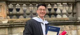 Alumnus Ben Tan at Old College holding graduation certificate and scroll
