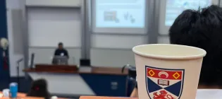 A University of St Andrews coffee cup in front of a conference session.